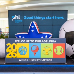 Sign on stage that says welcome to Philadelphia where history happens 2026. basketball, golf, soccer, and baseball icons