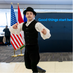 male dancer with black hat, black vest with white shits and black pants. Good things start here sign in background