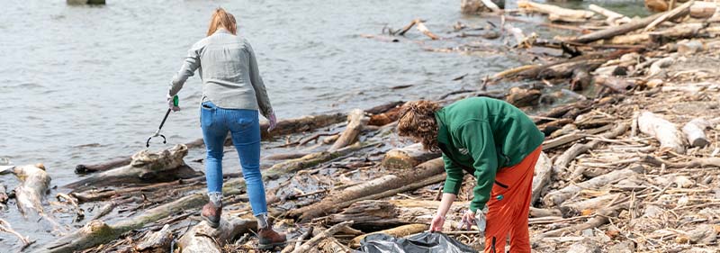 two people cleaning up trash by the water